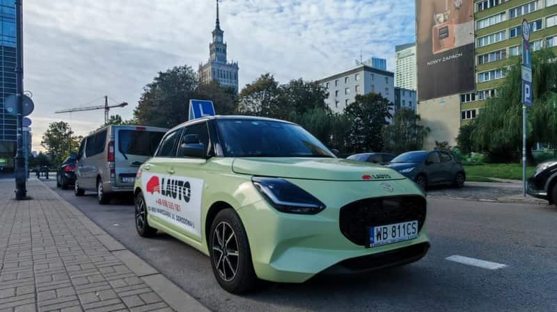Samochód szkoleniowy Suzuki Swift OSK Lauto z tablicą L w centrum Warszawy, w tle Pałac Kultury i Nauki